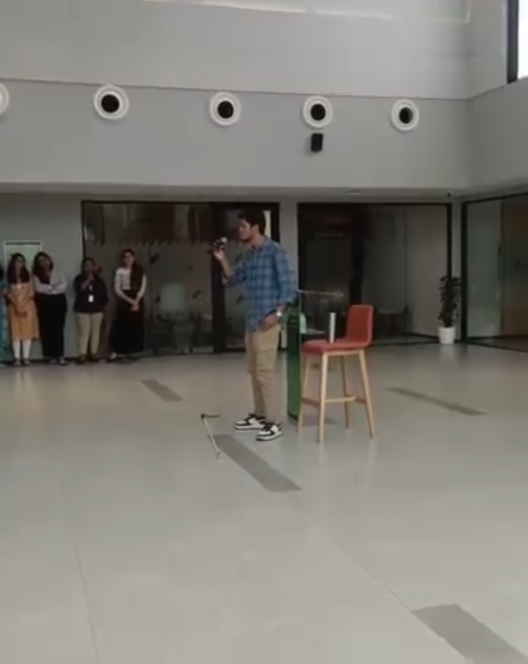 Bhavya is performing in a spacious corporate lobby, his cane lying on the floor in front of him and a podium and high stool behind him